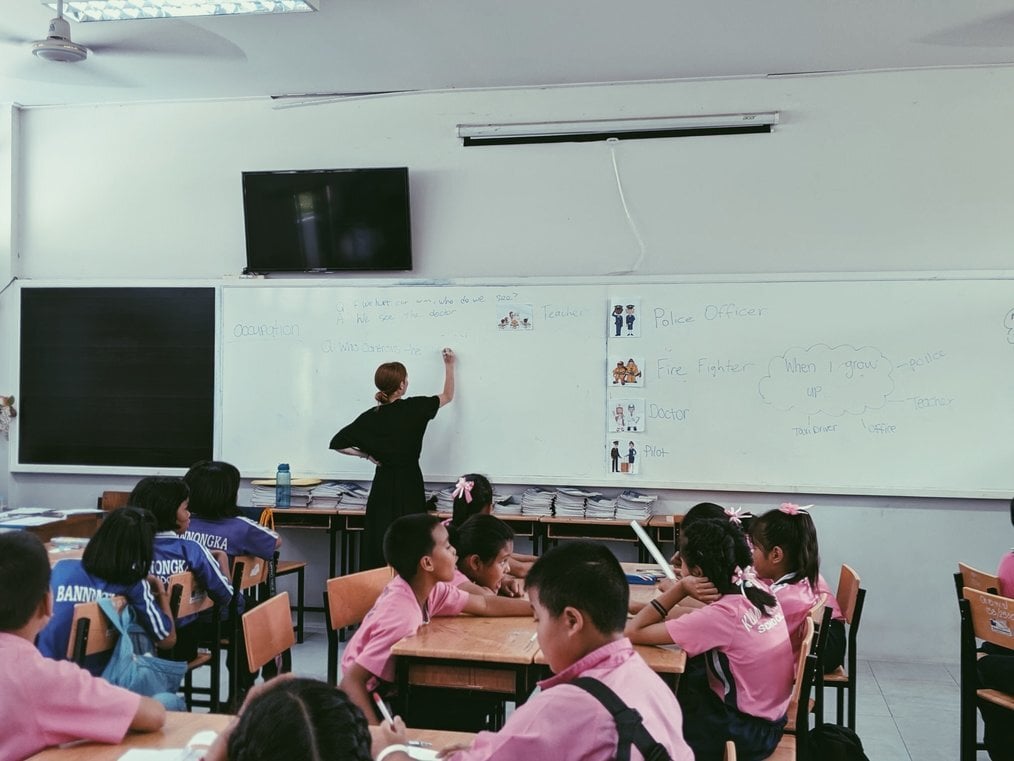 Greenheart Thailand A teacher writes on the board in a classroom full of young students.